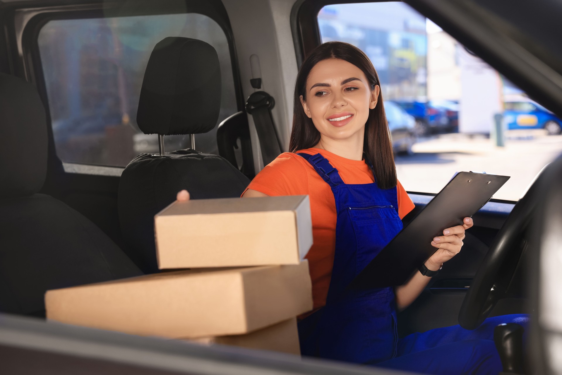Courier with clipboard checking packages in car